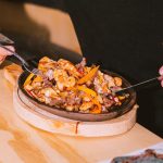 A man enjoying a hot plate of sizzling shrimp fajitas with vegetables indoors.